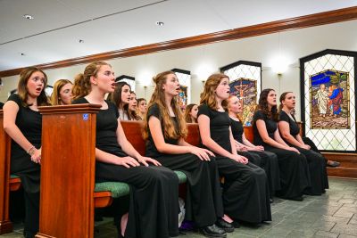 Singers seated in the pews singing beneath stained glass windows