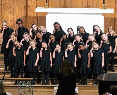 The youngest choir performing on risers with hands cupped to their ears