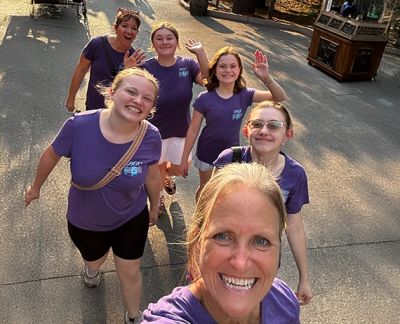 Singers and a chaperone smiling in a group selfie on a shaded walkway