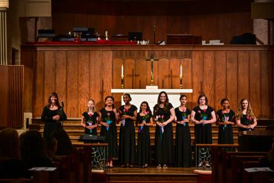 Graduating singers holding roses on the chancel steps with their director