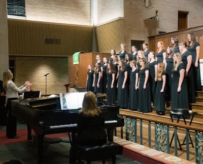The choir performing on risers beside a grand piano