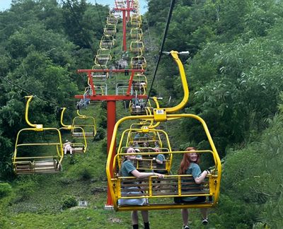 Two singers riding a chairlift above a wooded hillside