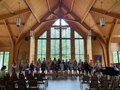 Campers rehearsing in a timber-framed chapel with a tall wall of windows