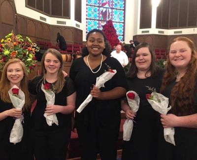 Five singers in concert black holding roses after a performance